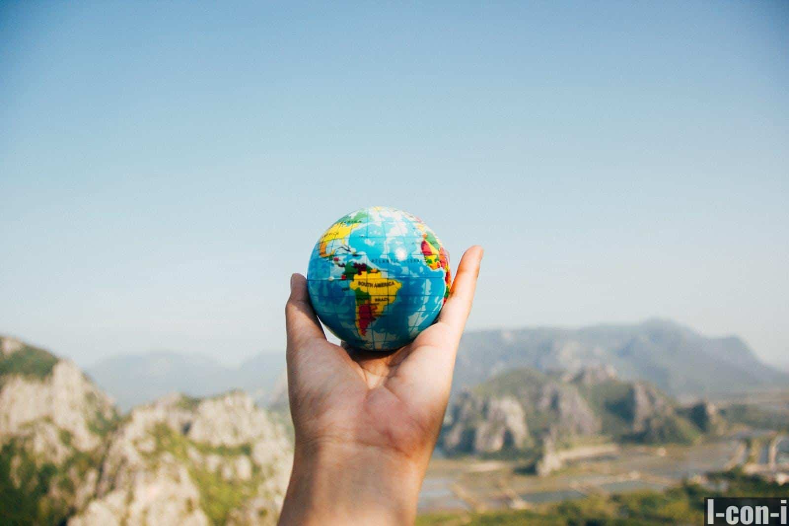 Person Holding World Globe Facing Mountain